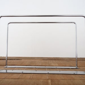 May include: Two chrome metal shelf brackets with a flat base and two vertical supports. The brackets are stacked on top of each other.