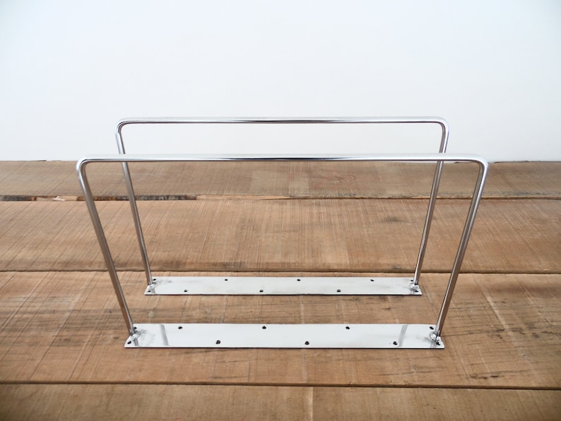 May include: Two silver metal shelf brackets with a rectangular base. The brackets are made of sturdy metal and are designed to support shelves.