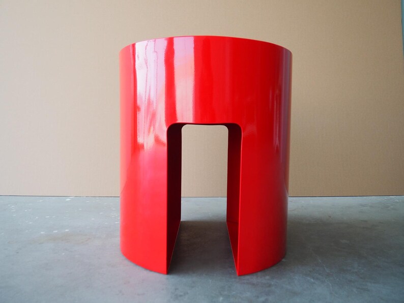 May include: A vibrant red, cylindrical side table with a glossy finish. The table has a cutout section in the center, creating an open space. The design is modern and minimalist, suitable for various interior settings.