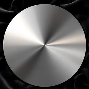 May include: A round, silver, metal disc with a brushed finish. The disc is lying on a black, silky fabric.