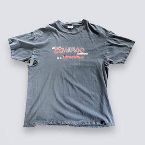 May include: A faded gray t-shirt with the text "Being a COMPAQ customer is a DirectPlus" in red and white. The shirt has short sleeves and a crew neck. The fabric appears worn and soft.