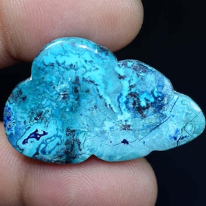 May include: A blue and black chrysocolla cabochon carved in the shape of a cloud. The stone has a unique, marbled pattern.