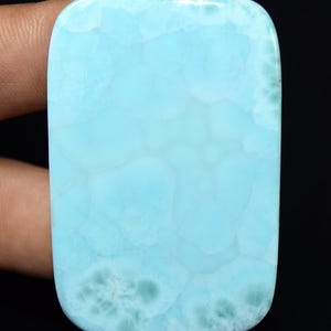 May include: A rectangular, polished gemstone with a light blue color and a unique, textured pattern. The stone has rounded corners and a smooth surface. The overall appearance is reminiscent of ocean water.