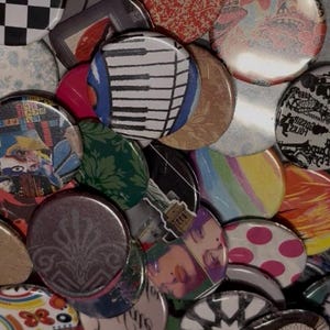 May include: A collection of colorful round buttons with various designs. The buttons feature patterns like a piano keyboard, checkered squares, floral prints, and abstract art. The color palette includes red, white, black, and shades of blue and green.