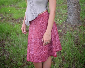 May include: A woman wearing a gray halter top with a lace trim and a red floral print skirt. She is standing in a forest setting.