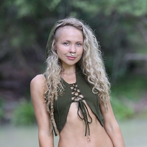 May include: A woman wearing a green hooded top with a lace-up front and black trousers with a belt. The top is cropped and shows her midriff. She has blonde hair and is wearing a nose ring.