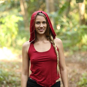 May include: A woman wearing a red hooded top and black shorts with a ruffled hem. She is standing in a woodland setting.