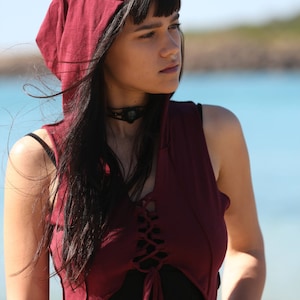 May include: A maroon hooded top with a lace-up front and a black skirt. The top is sleeveless and has a relaxed fit. The model is wearing a black choker necklace.