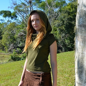May include: A woman wearing a green hooded top and a brown crochet skirt. She is standing in a grassy area with a tree trunk behind her. The skirt has a unique design with a frayed hem and a pocket on the side. The text "Nature Spirit" is visible on the tree trunk.