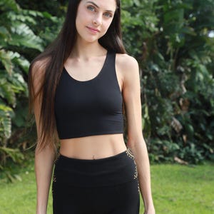 May include: Black athletic crop top and shorts set. The crop top has a scoop neck and racerback design. The shorts have a high waistband and a gold pattern on the sides. The set is made of a stretchy material.