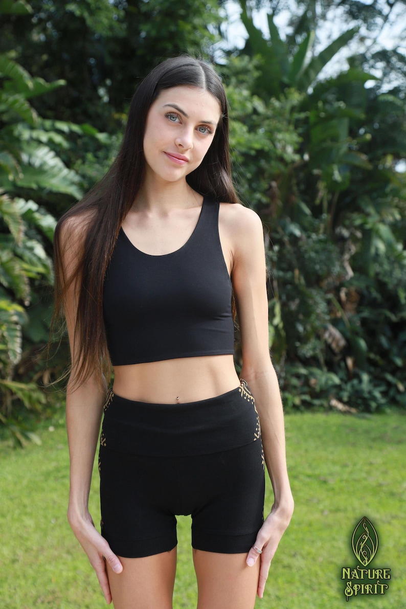 May include: Black athletic crop top and shorts set. The crop top has a scoop neck and racerback design. The shorts have a high waistband and a gold pattern on the sides. The set is made of a stretchy material.