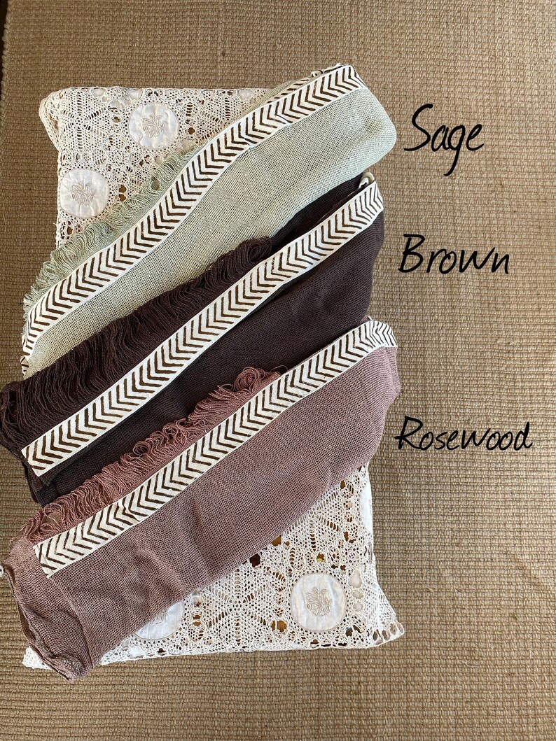 Pu&ograve; includere: Tre sciarpe con frange nei colori salvia, marrone e legno di rosa con un motivo a chevron bianco.