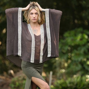 Pu&ograve; includere: Una donna indossa un kimono marrone con bordi bianchi a chevron e una gonna verde con spacco. &Egrave; in piedi in un'area erbosa con alberi sullo sfondo.