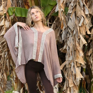 Pu&ograve; includere: Una donna indossa un poncho marrone con bordi a chevron bianco e marrone. Il poncho &egrave; realizzato in un tessuto morbido e leggero e ha una vestibilit&agrave; rilassata. Indossa anche leggings marroni con un motivo geometrico rosa e marrone.