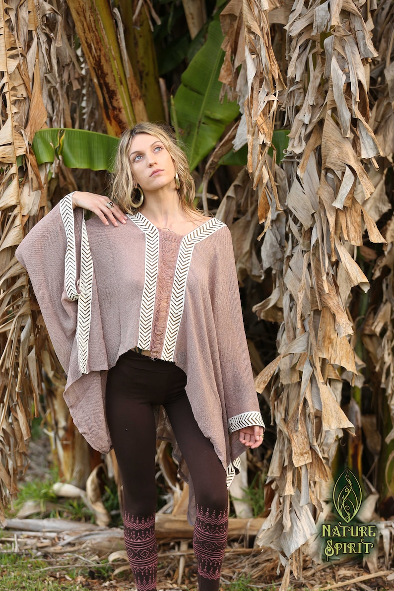 Pu&ograve; includere: Una donna indossa un poncho marrone con bordi a chevron bianco e marrone. Il poncho &egrave; realizzato in un tessuto morbido e leggero e ha una vestibilit&agrave; rilassata. Indossa anche leggings marroni con un motivo geometrico rosa e marrone.