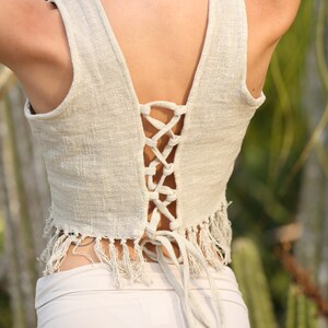 May include: A white crochet top with a lace-up back and fringe detail. The top is tied at the back with a long white string.