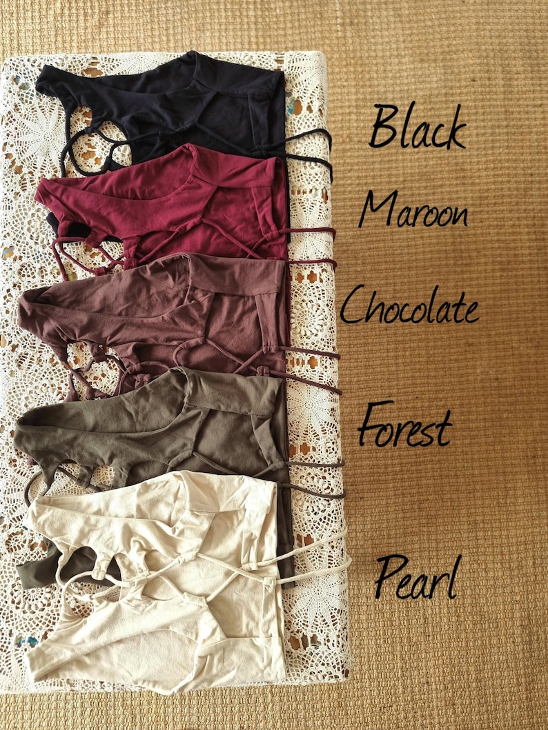 May include: Five tops in black, maroon, chocolate, forest green, and pearl. Each top has a crisscross design and is displayed on a white lace surface. The colours are labelled with handwritten text.