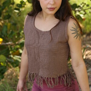 May include: A woman wearing a brown sleeveless top with fringe detailing and a pair of burgundy shorts with a geometric pattern. She has long brown hair and a nose ring.