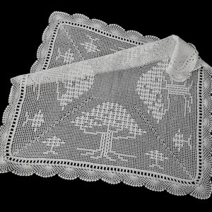 Könnte beinhalten: Eine weiße, gehäkelte Tischdecke mit einem gewellten Rand und komplizierten floralen und geometrischen Mustern. Die Tischdecke ist rechteckig mit einem gefalteten Abschnitt, der das filigrane Lochmusterdesign zeigt. Der Hintergrund ist schwarz.