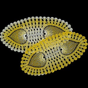 May include: Two handmade, oval-shaped crochet doilies. The doilies feature a spiral design in the center, with a scalloped edge. The color gradient transitions from white to yellow. The background is solid black.