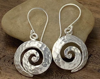 May include: A pair of silver earrings with a hammered finish and a spiral design. The earrings are hanging from a silver hook.