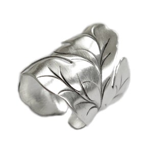 May include: A silver ring featuring a leaf design. The ring is made of metal and has a textured finish.