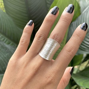 Peut inclure: Une bague en argent avec une large bande texturée. La bande est composée de nombreux fils fins empilés qui créent un effet ondulé.