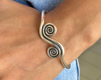May include: A silver bracelet with a wavy design and two spiral accents.