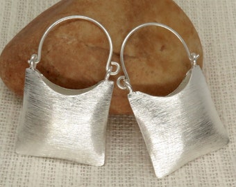 May include: A pair of silver-toned earrings. Each earring features a square, textured design with a curved top and a simple hook closure. The earrings are displayed against a neutral background.
