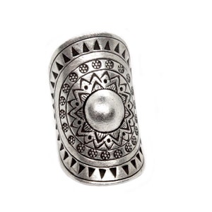 Puede incluir: Un anillo plateado con un diseño intrincado grabado. El anillo presenta un elemento circular central rodeado de patrones detallados de triángulos, círculos y motivos florales. El anillo tiene una banda ancha y una forma ligeramente curvada, sobre un fondo blanco.