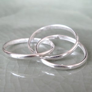 May include: Three interlocking silver rings, each with a smooth, polished finish. The rings are arranged in a triangular shape, creating a modern and minimalist design.