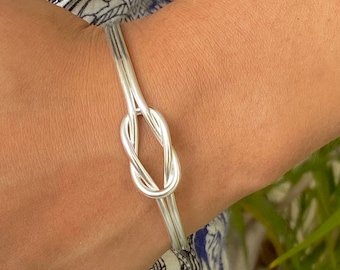 May include: A silver knot bracelet with a simple, elegant design. The bracelet is made of two strands of silver wire that are twisted together to form a knot.