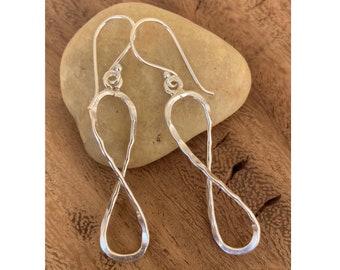 May include: A pair of silver infinity symbol earrings with a twisted design. The earrings are hanging from a wooden surface.