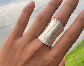 May include: A silver ring with a wide, textured band. The ring is made of many thin, stacked wires that create a unique, organic look.