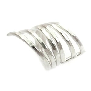 May include: Silver ear cuff with a hammered finish and a curved design. The cuff is made of multiple thin bands of metal that are stacked on top of each other.