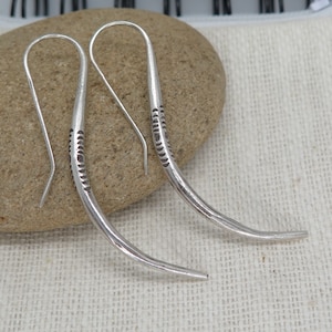 May include: A pair of silver earrings with a curved, textured design. The earrings are made of a thin, wire-like material and have a simple, minimalist style.