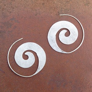 May include: A pair of silver hoop earrings with a spiral design. The earrings are made of metal and have a smooth finish.