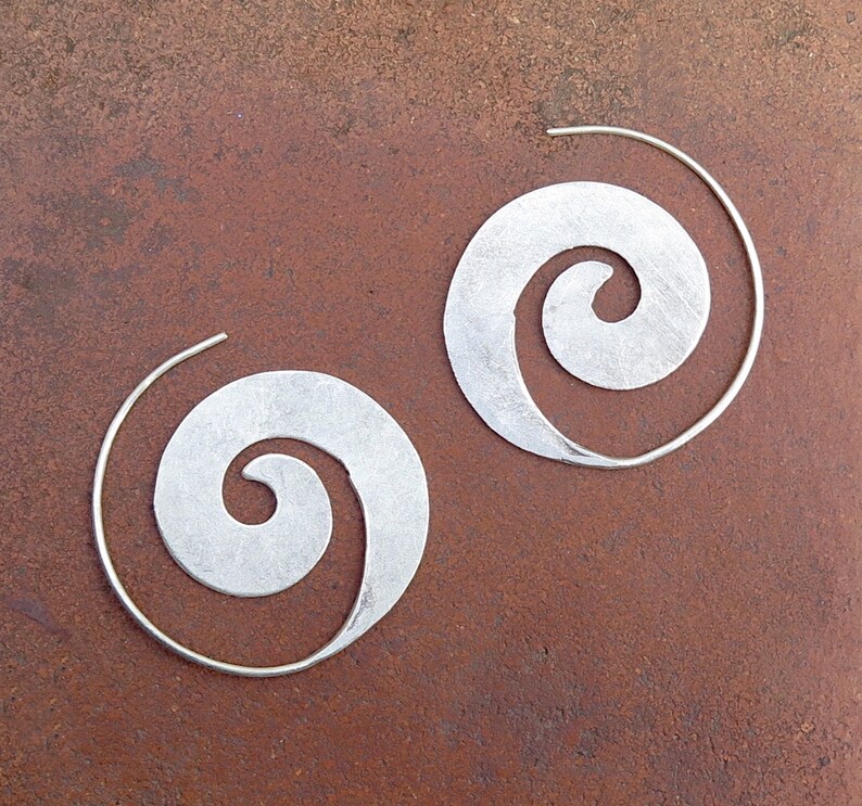 May include: A pair of silver hoop earrings with a spiral design. The earrings are made of metal and have a smooth finish.