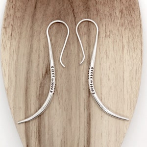 May include: A pair of silver hoop earrings with a curved, textured design. The earrings are made of sterling silver and have a simple, elegant style.