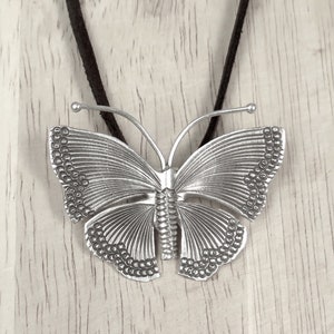 May include: A silver butterfly pendant necklace with a detailed design. The butterfly has a textured surface and is suspended from a black cord.