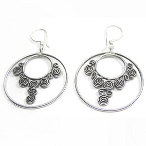 May include: Silver hoop earrings with a decorative design of swirling circles. The earrings are large and have a dangling charm.