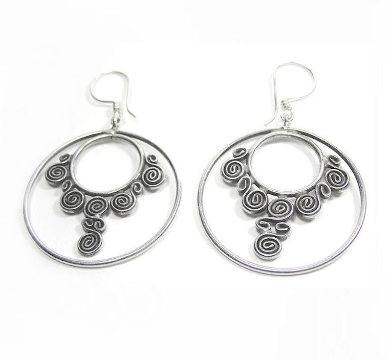 May include: Silver hoop earrings with a decorative design of swirling circles. The earrings are large and have a dangling charm.
