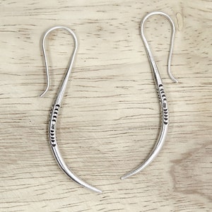 May include: A pair of silver hoop earrings with a textured design. The earrings are made of a thin, curved wire and have a hook closure.