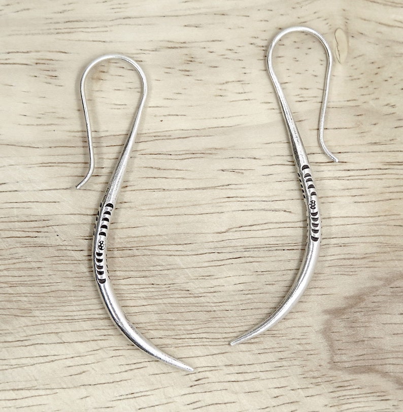 May include: A pair of silver hoop earrings with a textured design. The earrings are made of a thin, curved wire and have a hook closure.