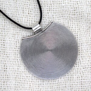 May include: A silver pendant necklace with a circular design featuring concentric circles. The pendant is attached to a black cord.