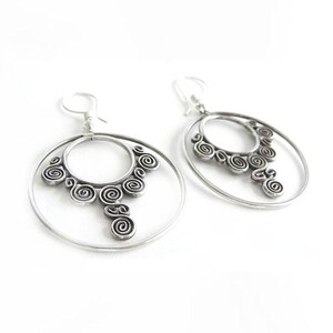 May include: Silver hoop earrings with a dangling spiral design. The earrings are made of metal and have a polished finish.