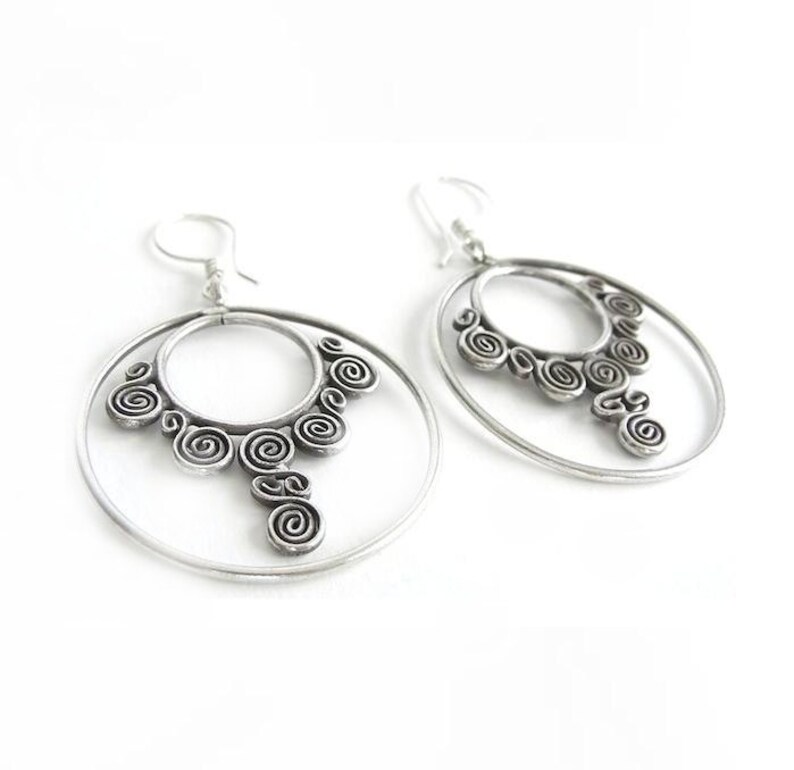 May include: Silver hoop earrings with a dangling spiral design. The earrings are made of metal and have a polished finish.