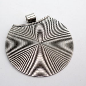 May include: Silver pendant with a circular design featuring concentric circles. The pendant has a loop at the top for attaching a chain.