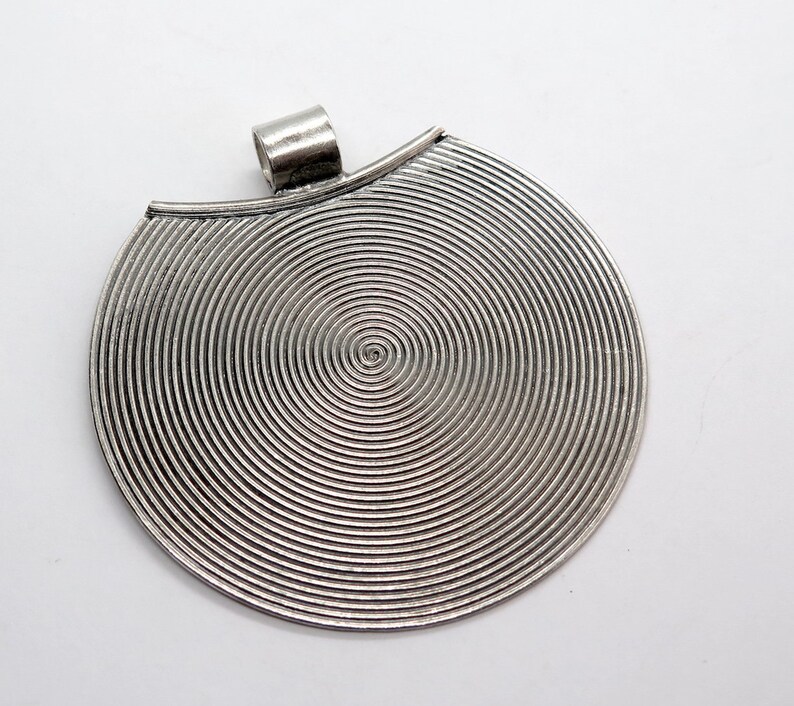 May include: Silver pendant with a circular design featuring concentric circles. The pendant has a loop at the top for attaching a chain.