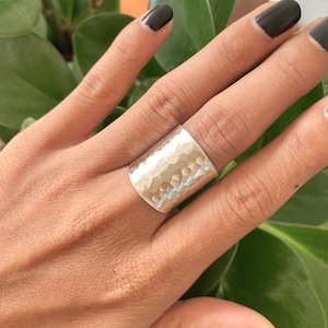 Op de afbeelding: Een brede, gehammerde zilveren ring. De ring is gemaakt van een dikke band metaal die is gehammerd om een ​​getextureerd oppervlak te creëren.